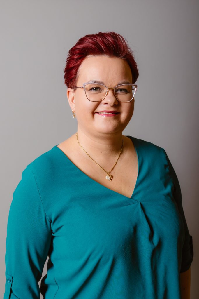 Starszy specjalista ds. jakości, Pełnomocnik ds. kontroli zarządczej. mgr Sylwia Draszek Kobieta w bordowych włosach, w okularach, w zielonej bluzce