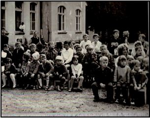 Czarno-białe zdjęcie przedstawia grupę dzieci siedzących na dziedzińcu szpitala
