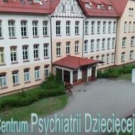 Zdjęcie przedstawia budynek główny szpitala, po prawej stronie widać dwa maszty z baneramy na których jest napis Ameryka. Na dole zdjęcia napis-Północne Centrum Psychiatrii Dziecięcej.