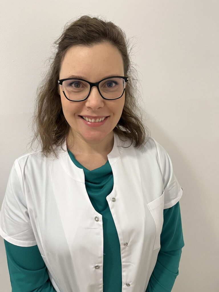 Asystent lek. Natalia Galińska-Liss
specjalista gastroenterologii dziecięcej. Kobieta ubrana w zieloną bluzkę na długi rękaw i biały kitel. Włosy brązowe do ramion rozpuszczone, czarne okulary, uśmiechnięta. 